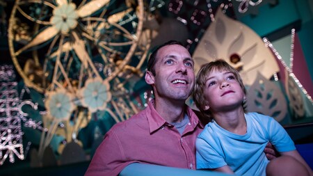 A father and son watch in wonder while cruising through “it’s a small world” at Magic Kingdom park