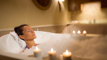 A woman relaxing with her eyes closed as she lies back in a bubble bath
