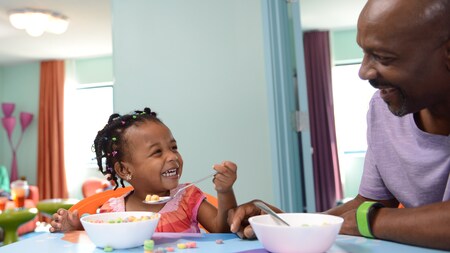 A father and his daughter laugh while enjoying a cereal breakfast together at a Disney Resort hotel