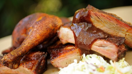 Slices of barbecue pork near half a chicken and a pile of coleslaw