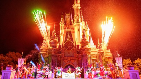 Mickey, Minnie, Pluto and more Disney characters stand on stage in front of Cinderella Castle holding a sign saying ‘Happy Holidays’