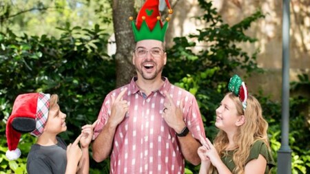A man and his 2 kids pose for a picture wearing elf hats.