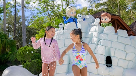 2 girls in bathing suits hold hands near statues of Anna and Elsa