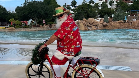 Santa in tropical clothing rides a bike through Disney’s Blizzard Beach