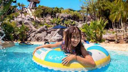 A girl floating on an inner tube in a pool surrounded by palm trees and tropical plants