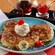 Pancakes shaped like Mickey ears topped with sprinkles, syrup, whipped cream and cherries plus a plastic insignia that says Chef Mickeys and jars with 3 toppings