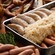 Pan filled with sauerkraut and 2 types of German sausages sitting on a table next to meats and pretzels