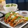 Tacos from Level99 Disney Springs topped with cheese, guacamole and cilantro served on a tray alongside glazed skewers and a grain bowl