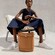 A woman seated in a chair wearing Cole Haan sneakers with a leather bucket bag at her feet