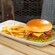 A bacon cheeseburger atop a tomato slice and lettuce, with a side of fries