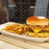 A beef burger topped with pulled pork, cheese, coleslaw and barbecue sauce, with a side of fries