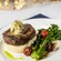 A plated Grilled Filet Mignon featuring a grilled steak topped with butter, served on mashed potatoes with roasted broccolini and cherry tomatoes