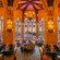 A grand dining room with high arched ceilings, stained glass windows, chandeliers and tables set for Guests