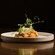 A plated dish of burrata topped with herbs and pea shoots, served over sautéed shrimp and vegetables