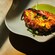 A charred octopus tentacle served over a purée with leafy greens on a curved ceramic plate