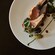 Two lamb chops on a plate, garnished with blackberries, fresh herbs and a drizzle of sauce