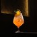 An iced cocktail in a stemmed wine glass garnished with an orange wedge and mint leaves