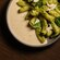 A ceramic dish of rigatoni pasta coated in pesto and topped with torn burrata and fresh basil leaves