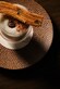 A glass filled with tiramisu, dusted with cocoa powder, topped with a single espresso bean and served with a churro resting across the rim