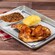 A half rotisserie chicken served with baked beans and a cornbread muffin on a tray