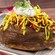 A loaded baked potato topped with chili, cheese, sour cream and avocado sauce