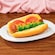 A plant based food item in the shape of a hotdog, with tomatoes, mustard, aioli and green relish on a bun