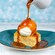 Coconut pineapple bread pudding with caramel sauce being poured from a pitcher over a dollop of cream from Sebastian's Bistro