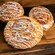 A Mickey Mouse shaped Cinnamon Roll drizzled with white icing on a wooden surface