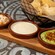 A basket of chips next to a serving board with roasted corn, queso and guacamole dips