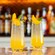 Two beverages garnished with fruit and mint sit on a bar