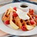 Waffles topped with cream served on a plate with fruit, bacon and syrup
