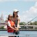 A girl wearing a life vest casts a fishing line with support from her mother