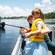 A girl holds a fishing pole in the water over the railing of a boat as her mother watches