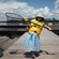 A young girl with a fishing hat and a life vest stands on a dock with a fishing net that holds her catch