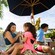 A mother and young daughter laughing together on a beach lounge chair surrounded by tropical greenery