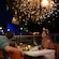 A family of 4 dine on an outdoor terrace as fireworks burst above Cinderella Castle in the background