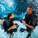 A teenage girl and her father, both in wetsuits and scuba gear standing waist deep in a pool   