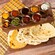 An array of 10 sauces on a tray next to a plate of naan bread