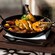 A cast iron pan filled with saffron rice, roasted chicken, whole prawns and chorizo, served on a wooden board