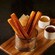 Cinnamon sugar churros in a basket on a board with 2 bowls of sauces