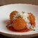 Three fried arancini over tomato sauce, topped with shaved cheese and herbs on a plate