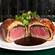 Beef Wellington sliced open to reveal a beef fillet encased in a mushroom duxelles and puff pastry, served on a plate with a jus and a garnish of microgreens