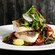 A branzino fillet stacked over mushrooms and a sauce, topped with radish slices, chives, red cabbage microgreens and herbs