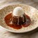 A sticky toffee pudding served in a bowl with toffee sauce and topped with a scoop of vanilla ice cream