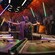 A character stands with arms outstretched as Guests raise their glowing lightsabers   