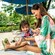 Mother and young daughter sit under an umbrella in a lounge chair on a beach