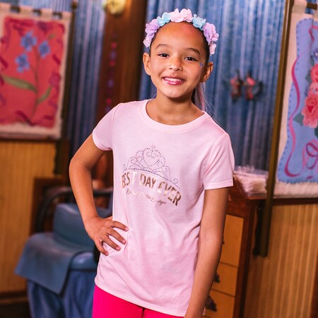 A girl wears a flowered headband in her hair and a shirt that says ‘Best Day Ever’