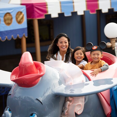 A little boy wearing Mickey Ears rides Dumbo the Flying Elephant with his mom and sister