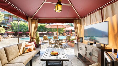 A long, poolside cabana with furniture, a flat screen television, an overhead lantern and ceiling fan
