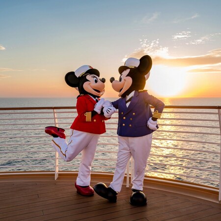 Captains Minnie Mouse and Mickey Mouse smiling at each other on the top deck of a Disney cruise ship at sunset